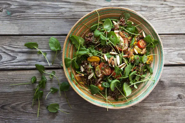 En härlig quinoa sallad med körsbärstomater, gröna blad och mandelspån, serverad i en vacker skål på en träbakgrund.