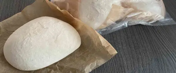 Frische Pizzaböden, bereit für das Pizzateig einfrieren. Einer liegt auf Backpapier, weitere sind in Folie verpackt.