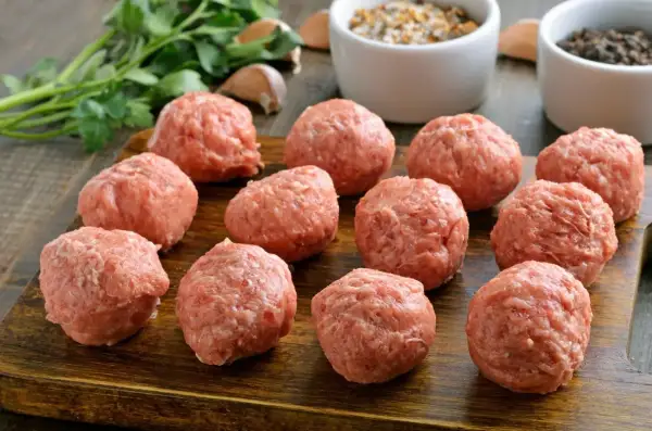 Gotowe do smażenia, obłędne kotlety mielone. Na drewnianej desce leży kilkanaście okrągłych porcji mięsa mielonego, obok pęczek natki pietruszki i czosnek.