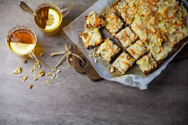 En härlig vegansk morotskaka med glasyr, nötter och citrusskal. Två koppar te med citron står bredvid.