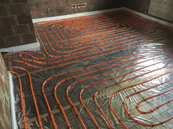 Pomarańczowe rury ogrzewania podłogowego ułożone na folii, przygotowane do wylania betonu. To kluczowy etap hydroizolacji chudziaka.
