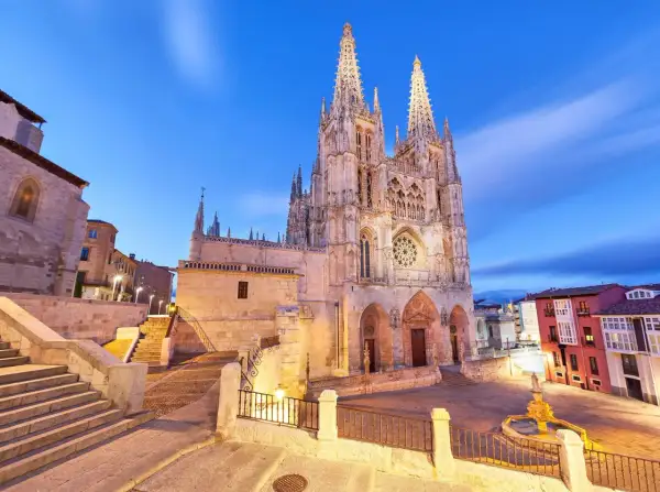 Majestuosa catedral de Burgos al anochecer, con sus agujas góticas iluminadas y el cielo azul crepuscular.