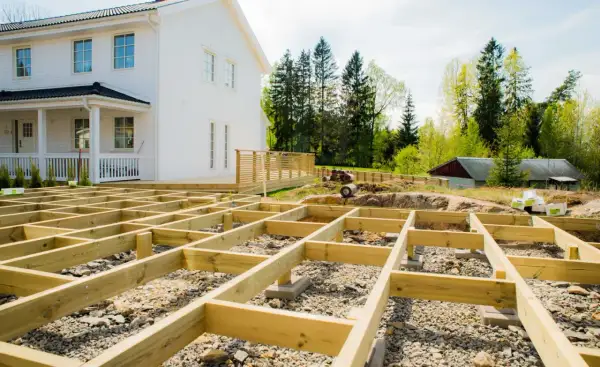 Grundarbete för att bygga altan på mark. Träkonstruktionen är på plats framför ett vitt hus.