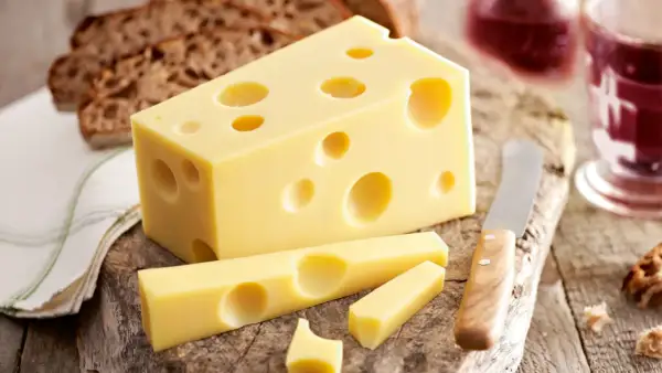 Ein Stück Emmentaler mit seinen charakteristischen Löchern, daneben Brot und ein Glas Rotwein. Die Herkunft des Käses ist unverkennbar.