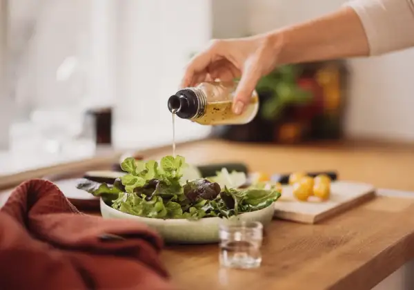 Frische Salatblätter werden mit einem Dressing beträufelt. Rotweinessig ist eine gesunde Wahl, besonders in der Schwangerschaft.