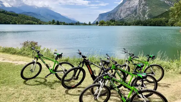 Biciclette verdi pronte per un'avventura sul lungolago di Riva del Garda, con montagne maestose sullo sfondo.