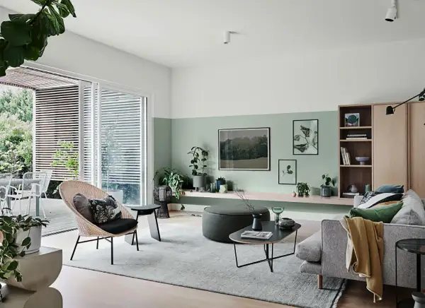 Soggiorno moderno con pareti bicolore, la parte inferiore dipinta in un rilassante verde salvia colore pareti, arredi minimalisti e piante.