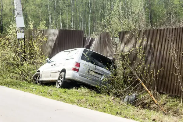 Srebrny minivan wjechał w drewniane ogrodzenie, powodując jego uszkodzenie. Pojazd jest częściowo wciśnięty w płot.