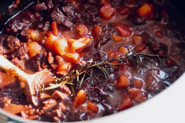 Herzhaftes Rindfleisch mit Tomaten und Rosmarin köchelt in einem Topf. Ein Holzkochlöffel rührt in der Soße. Perfekt für ein Bolognese Rezept.