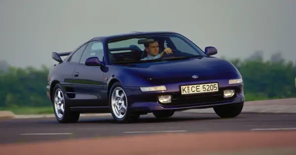 Mężczyzna prowadzi fioletowe Toyota MR2 SW20 po krętej drodze.