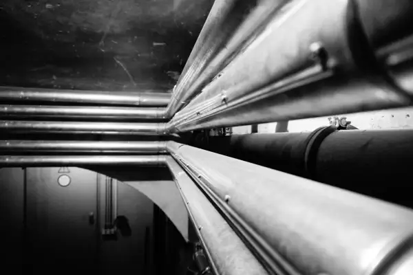 Mehrere Heizungsrohre werden in einem dunklen Raum verlegt. Sie verlaufen parallel und bilden ein komplexes Netzwerk.