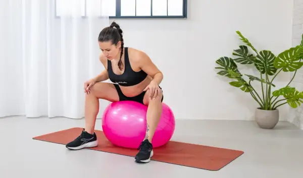 Mujer embarazada sentada en una pelota de ejercicio rosa, preparándose para fortalecer el suelo pélvico.