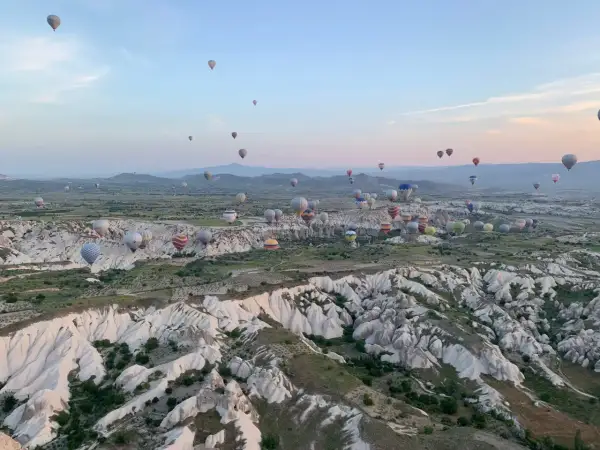 Setki balonów na gorące powietrze unoszą się nad skalistym krajobrazem Kapadocji o wschodzie słońca. To marzenie o podróżowaniu, które można zrealizować, szukając sposobów, jak tanio podróżować.