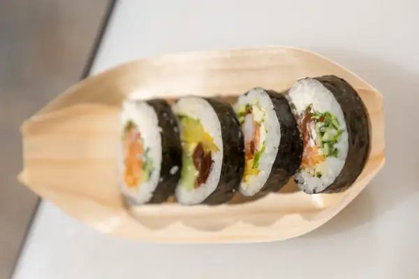 Pięć kawałków sushi z łososiem, awokado i krewetkami na drewnianej łódce. Różne rodzaje sushi nazwy w zasięgu ręki.