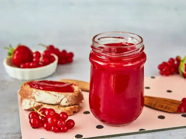 Glas mit Erdbeer Johannisbeer Marmelade, daneben Brot mit Marmelade und frische Beeren.