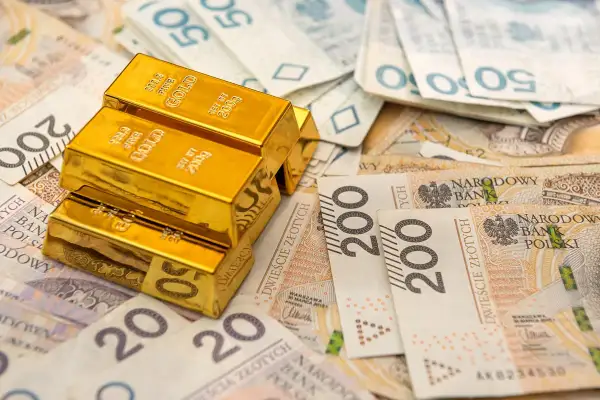 Sztabki złota na stosie polskich banknotów. Rozważasz sprzedaż złota i zastanawiasz się nad podatkiem?