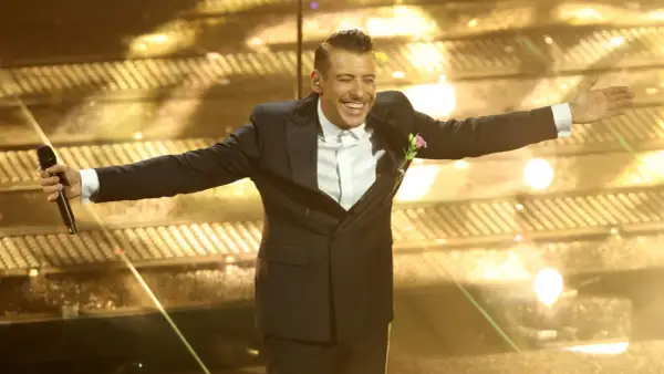 Un artista sorridente sul palco di Sanremo, con microfono in mano, pronto per i duetti.