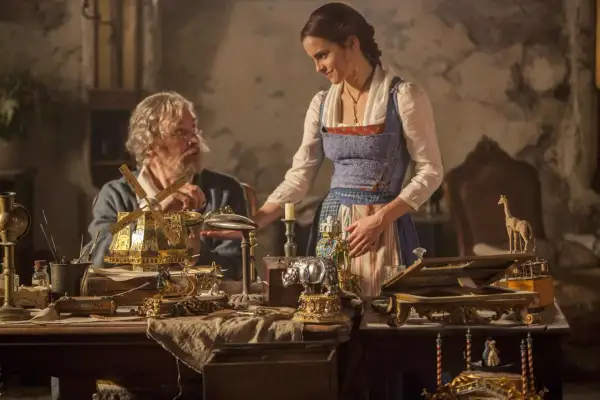 Bella y su padre, Maurice, observan un intrincado molino de viento dorado. La escena evoca la magia de "la bella y la bestia".