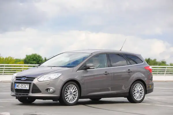 Szary Ford Focus MK3 kombi, z widocznymi reflektorami i felgami. Idealny do miasta i na wakacje, z pewnością z dobrymi żarówkami.