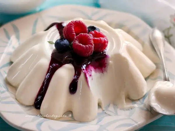 Deliziosa panna cotta con frutti di bosco e salsa ai mirtilli, servita su un piatto decorato.