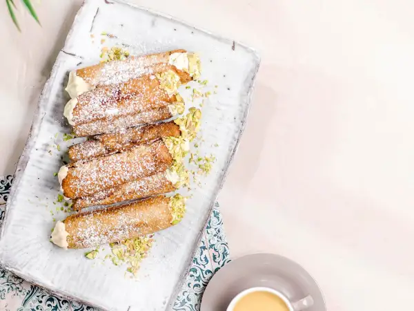 En bricka med flera italienska bakelser, cannolis, pudrade med florsocker och garnerade med hackade pistagenötter.