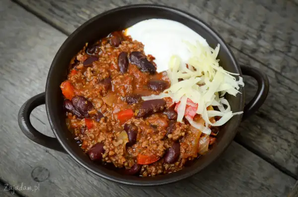 Pyszne chili con carne przepis: sycące danie z mielonym mięsem, fasolą i warzywami, podane z kwaśną śmietaną i startym serem.