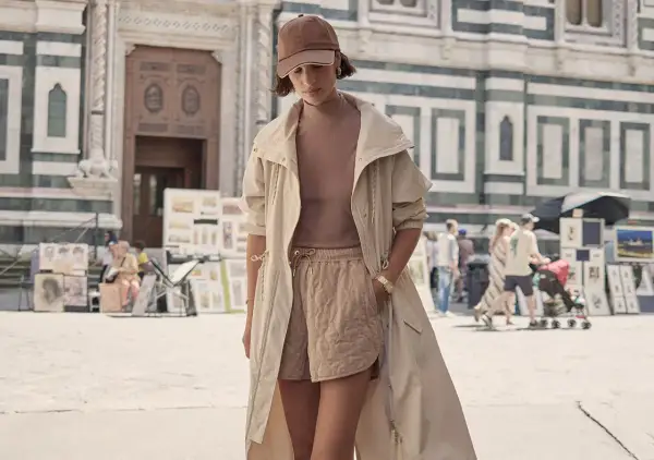 Frau im Athleisure Style mit beiger Jacke und gesteppten Shorts vor einer historischen Fassade.