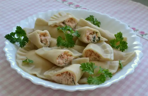 Pyszne pierogi z łososiem, delikatnie ugotowane, podane na białym talerzu z natką pietruszki.