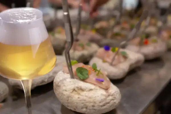 Un bicchiere di birre ale italiane accanto a tartare di pesce su pietre.