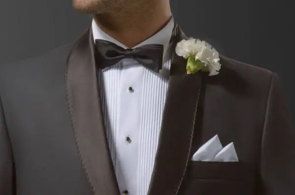 Elegancki mężczyzna w smokingu z czarną muszką i białą butonierką. W kieszeni marynarki biała poszetka.
