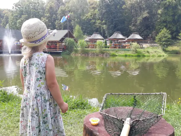 Dziewczynka w słomkowym kapeluszu patrzy na łowisko na wyspie Pokrzywna. Obok niej leży podbierak i kukurydza.