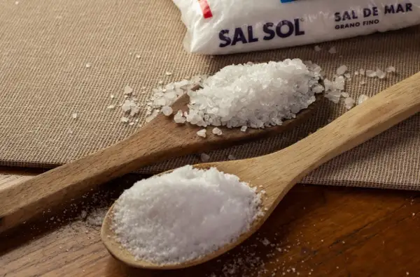 Dos cucharas de madera muestran cómo se obtiene la sal: una con sal marina gruesa y otra con sal fina, junto a un paquete de Sal Sol.