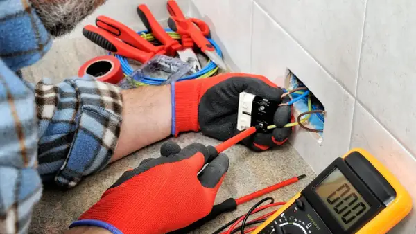 Un électricien utilise des outils pour installer une prise. On voit des fils, un tournevis, un multimètre et d'autres outils pour électricien.