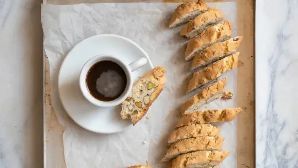 En kopp kaffe bredvid en rad med italiensk mandelskorpa, bakad med nötter och pistagenötter.