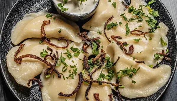 Pyszne pierogi ukraińskie, polane skwarkami i posypane natką pietruszki, podane z kwaśną śmietaną.