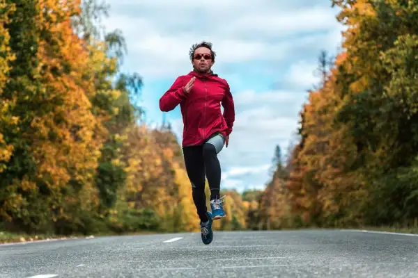 Un homme court sur une route bordée d'arbres aux couleurs d'automne, en plein effort, comme lors d'une séance fractionné.