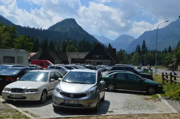 Na łysa polana parking, pełen samochodów, z górami w tle.