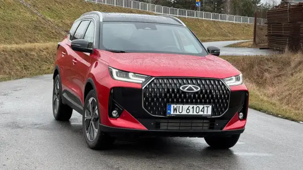 Czerwone auto Chery z czarnym grillem i felgami stoi na mokrej drodze.