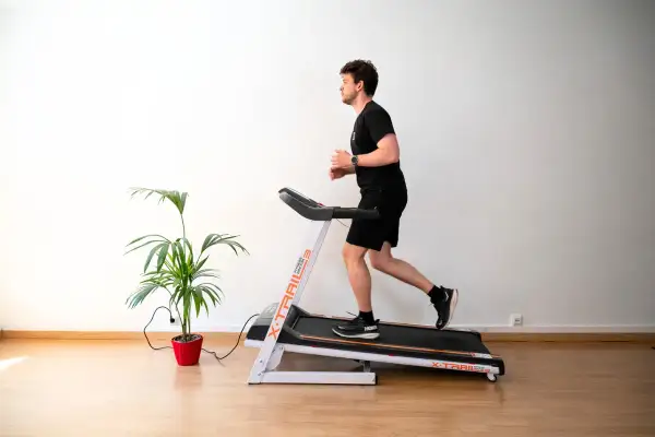 Un homme court sur un tapis de course, suivant un programme d'entraînement. Une plante verte décore la pièce.