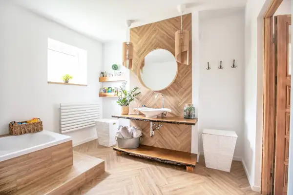 Salle de bain moderne avec sol et murs en bois, baignoire, lavabo et miroir. On peut mettre du parquet dans une salle de bain si le matériau est adapté.