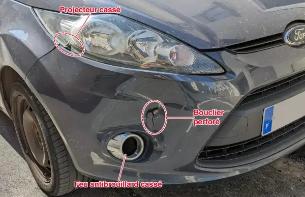 Avant le contrôle technique : feu antibrouillard avant cassé, bouclier perforé et projecteur endommagé sur une voiture grise.