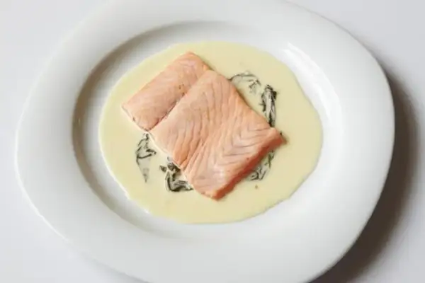 Deux pavés de saumon poêlés, nappés d'une onctueuse sauce oseille, servis sur une assiette blanche.
