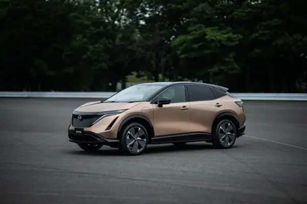 Elegancki, brązowy Nissan Ariya na tle zielonych drzew i asfaltu.