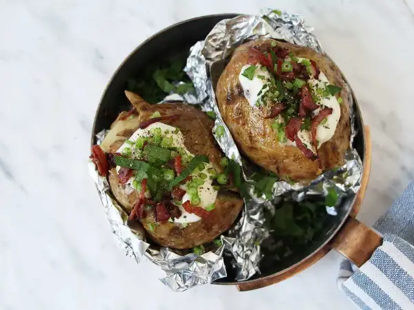 Två härliga bakade potatisar med gräddfil, knaperstekt bacon och gräslök i en kopparpanna.