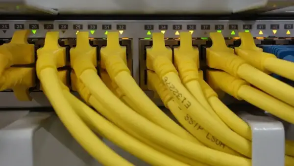 Conectores amarillos de red en un panel, cada uno con una luz verde o naranja encendida. Parece un splitter de red.