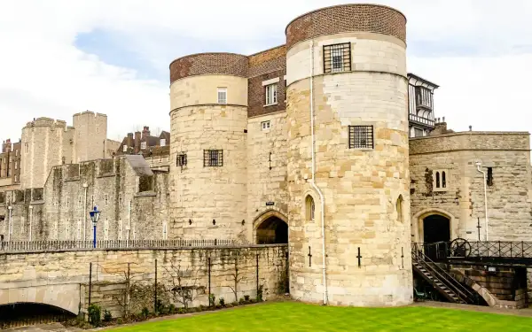 Kamienne wieże Tower of London, pełne ciekawostek, z kratami w oknach i zielonym trawnikiem.