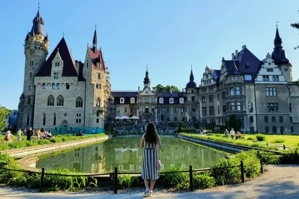 Kobieta podziwia zamek Moszna, jedną z największych atrakcji Opolszczyzny. Wspaniała architektura i staw tworzą malowniczy widok.