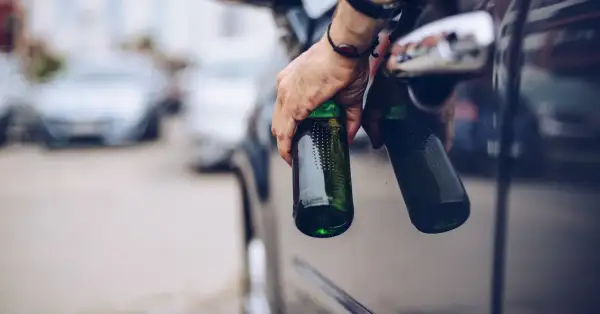 Hand hält Bierflaschen aus Autofenster. Die Frage "ab wie viel Promille ist man besoffen" wird hier thematisiert.