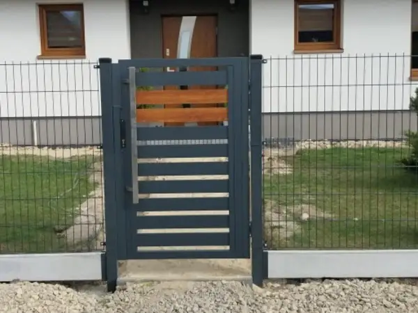 Nowoczesna furtka z metalu i drewna, osadzona na betonowym łączniku podmurówki.