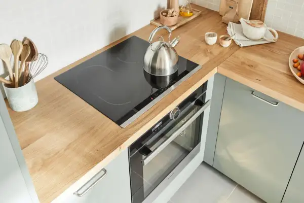 Un bollitore d'acciaio su un piano cottura a induzione in una cucina senza cappa. Utensili in legno in un contenitore.